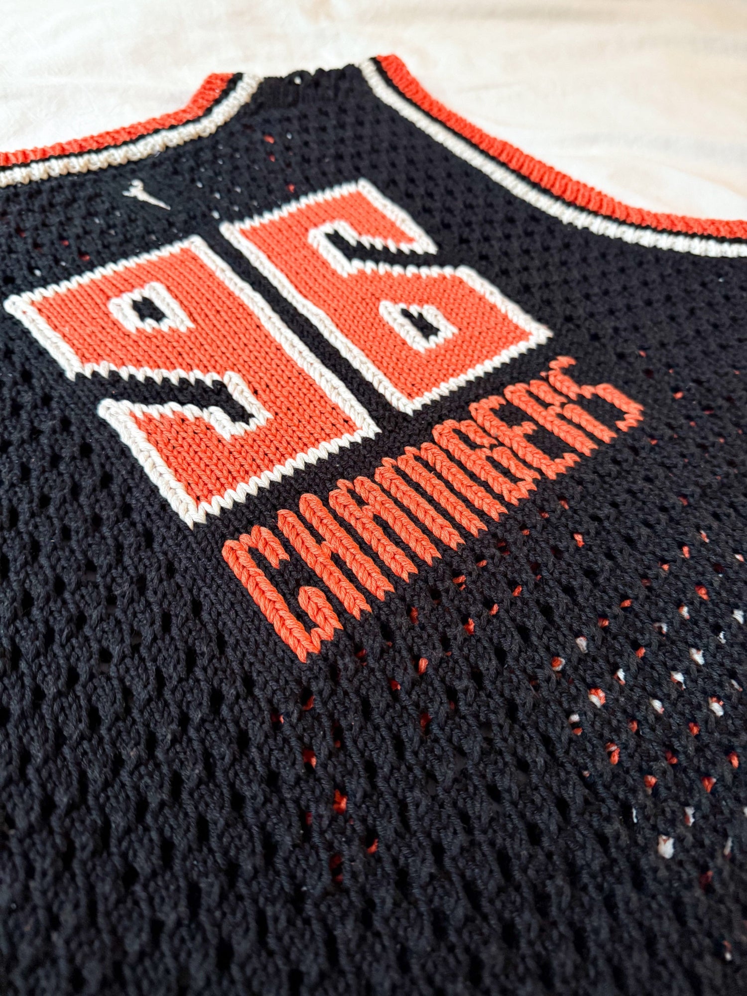 Black sports jersey with orange and white text and numbers on a light background